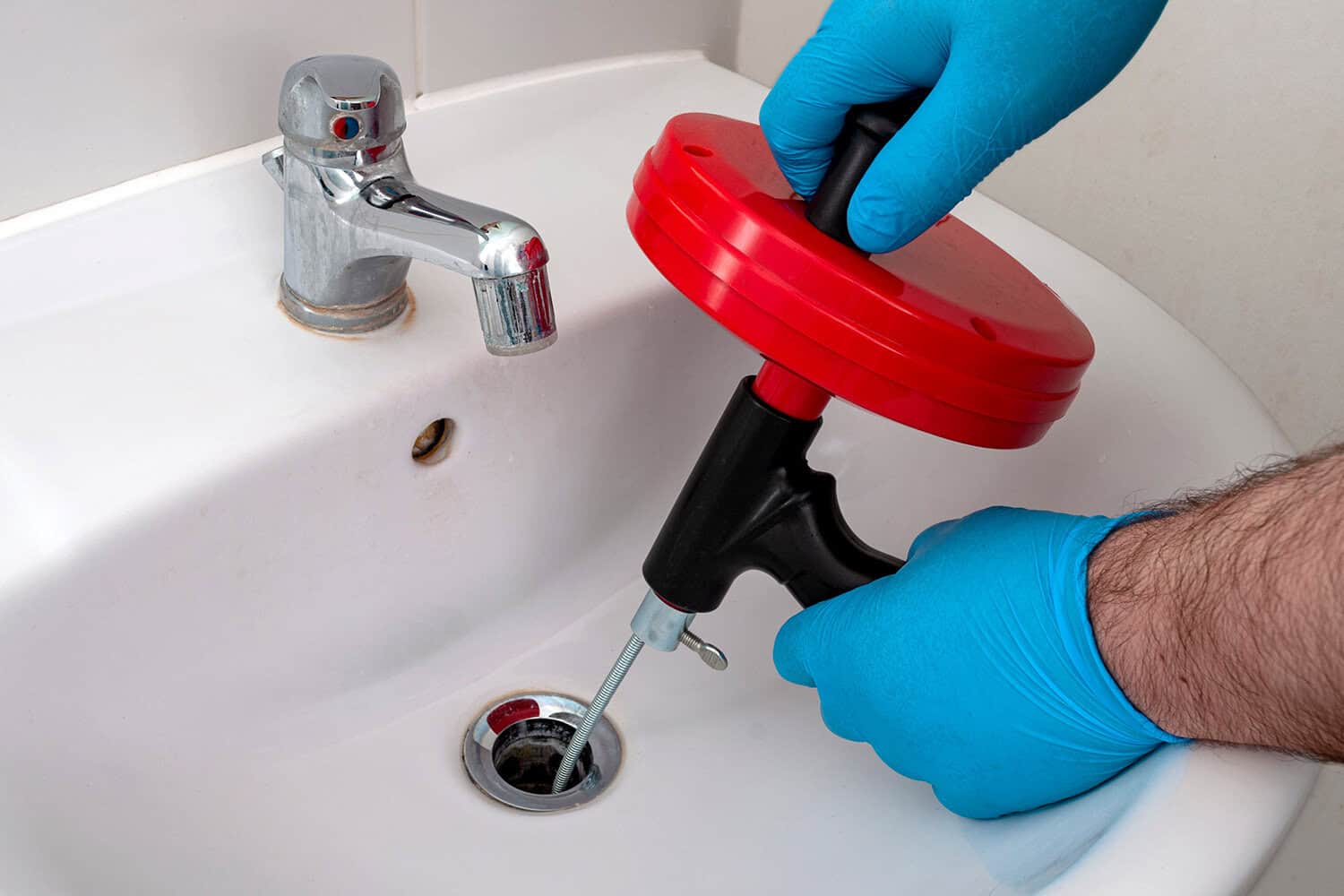 Professional drain cleaning with plumbing snake in bathroom sink.