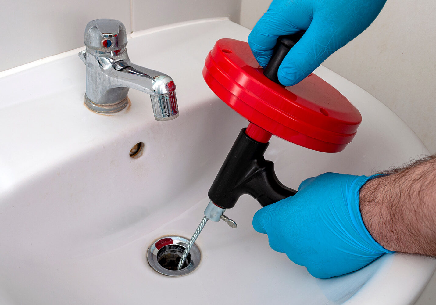 Professional drain cleaning with plumbing snake in bathroom sink.