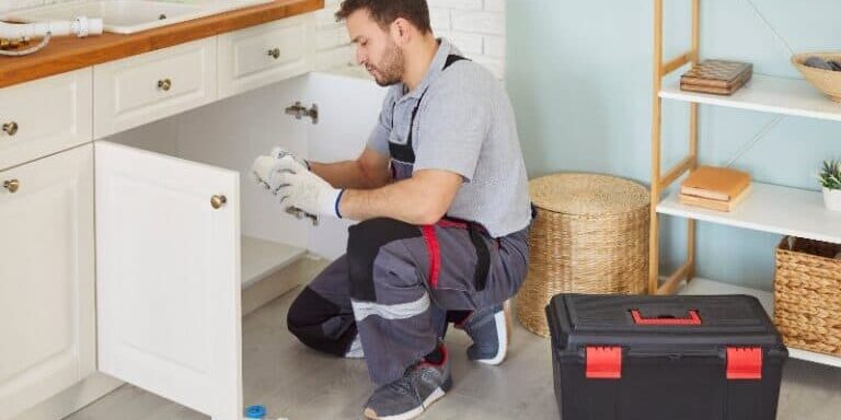 Professional licensed plumber changing pipes under a kitchen sink