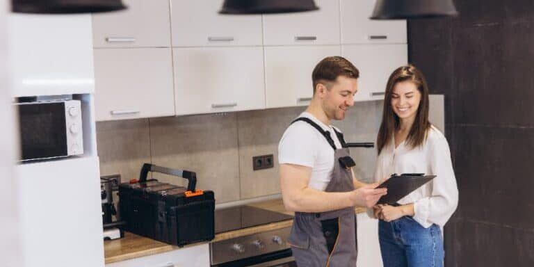 Smiling plumber presenting a repair estimate to a homeowner in a kitchen