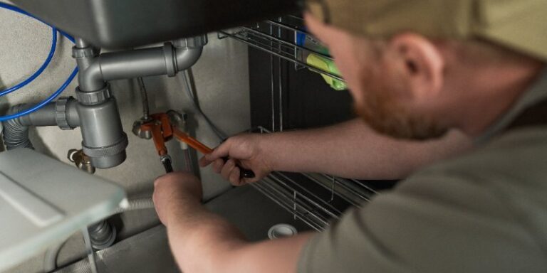 Experienced plumber repairing kitchen sink plumbing with a wrench